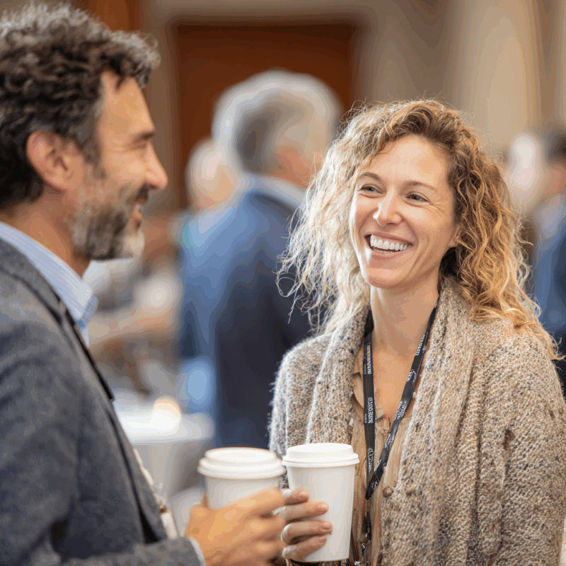 Two professionals laughing while holding coffee cups at a conference